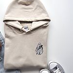 Sand Gildan 18500 hoodie embroidered with a little white ghost hugging a black cat on the left chest
