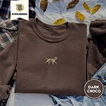 Dark Chocolate crewneck sweatshirt on a plaid flannel shirt with yellow autumn leaves and denim shorts, embroidered with a mini apricot goldendoodle trotting in a gold collar with its tongue out, in the center of the chest