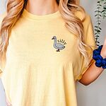 Woman in a Butter yellow T-shirt holding a scrunchie, embroidered with a small white goose and the word silly