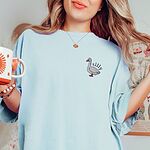 Woman holding a mug in a Chambray T-shirt embroidered with a small white goose and the word silly