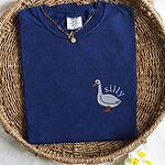 True Navy T-shirt folded in a woven basket, embroidered with a white goose and the word silly in white thread