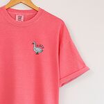 Watermelon T-shirt hanging on a wooden hanger, embroidered with a small white goose and the word silly