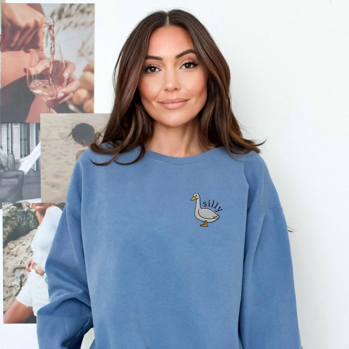 Embroidered Goose Sweatshirt - worn in blue Woman standing in a blue crewneck sweatshirt embroidered with a small white goose and the word silly on the left chest
