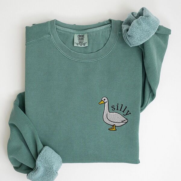 Embroidered goose sweatshirt in Light Green laid flat with rolled cuffs, stitched with a little white goose with the word silly arched over its back on the left chest