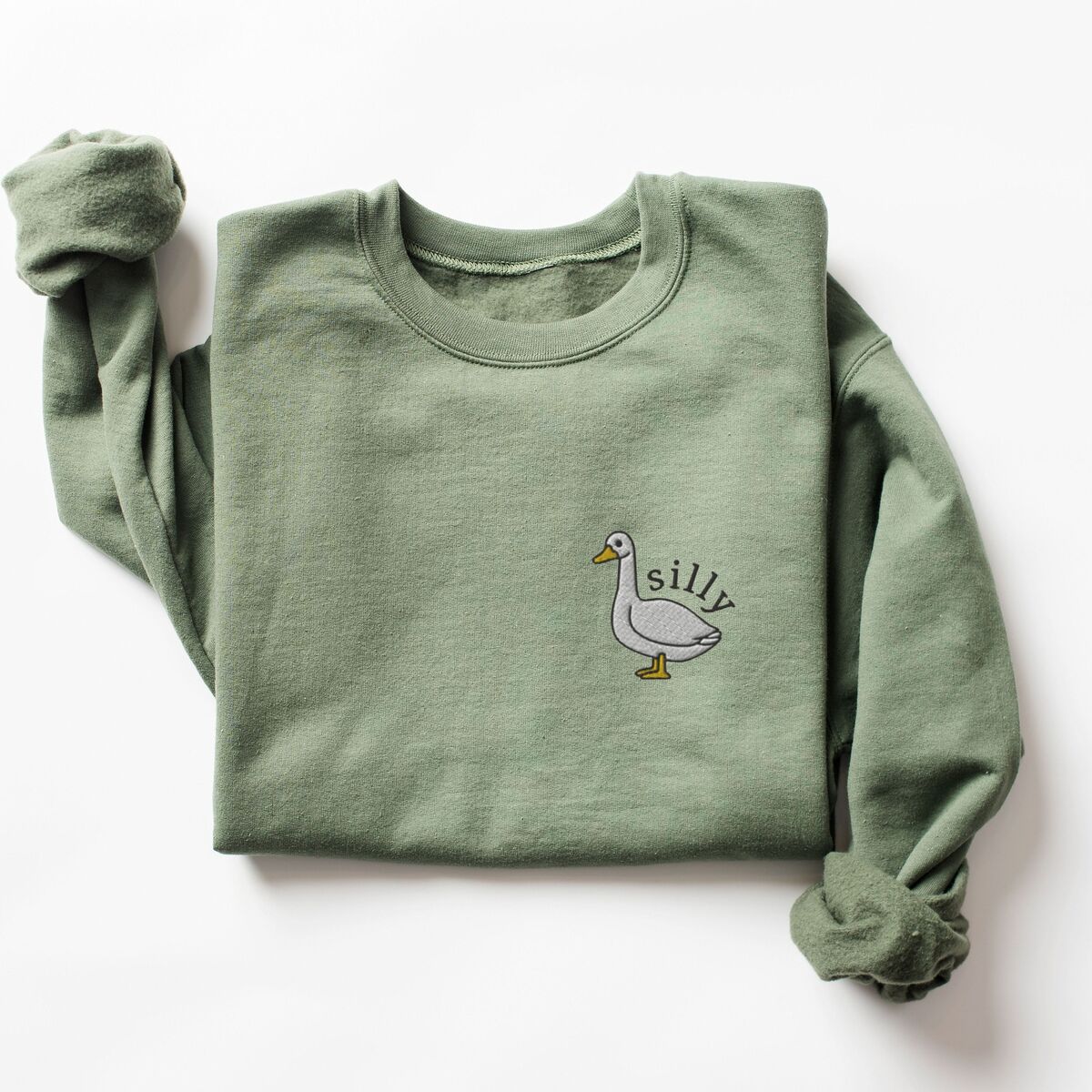 Embroidered Goose Sweatshirt - Military Green Military Green crewneck sweatshirt laid flat with a rolled sleeve, embroidered with a little white goose with the word silly arched over its back on the left chest