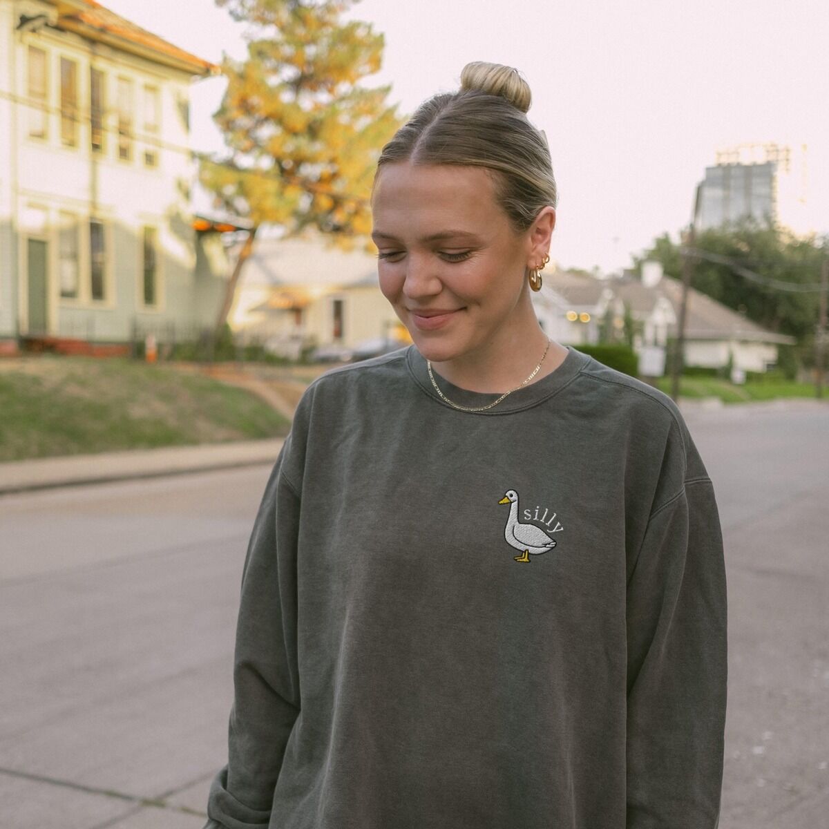 Embroidered Goose Sweatshirt – Pepper Woman walking down a street in a Pepper crewneck sweatshirt embroidered with a small white goose and the word silly