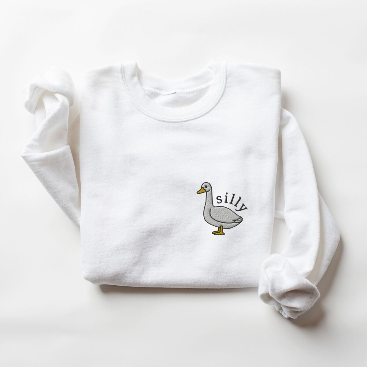Embroidered Goose Sweatshirt - White White crewneck sweatshirt laid flat with a rolled cuff, embroidered with a little white goose with the word silly arched over its back on the left chest