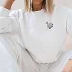 Woman relaxing in a White crewneck sweatshirt embroidered with a small white goose and the word silly on the left chest