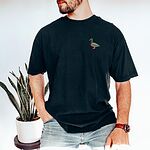 Man leaning on a stool beside a snake plant in a Black T-shirt embroidered with a small drake mallard