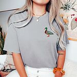 Woman in a Grey T-shirt and a gold necklace, embroidered with a drake mallard on the left chest