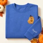 Embroidered Pomeranian Halloween sweatshirt in Heather Deep Royal with a witch-hat Pomeranian holding a pumpkin bucket on the left chest and the name Peanut on the left sleeve