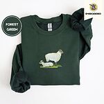 Forest Green crewneck sweatshirt folded on a white background, embroidered with a woolly white ewe standing over her lamb resting on a patch of green grass