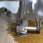Embroidery machine stitching a design in gold thread, from our video of how a design is digitized, machine-embroidered and finished