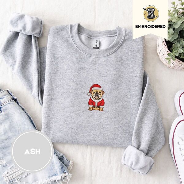 Ash crewneck sweatshirt folded with denim shorts, white sneakers and a potted plant, embroidered with a fawn English bulldog in a red Santa suit, black belt and Santa hat