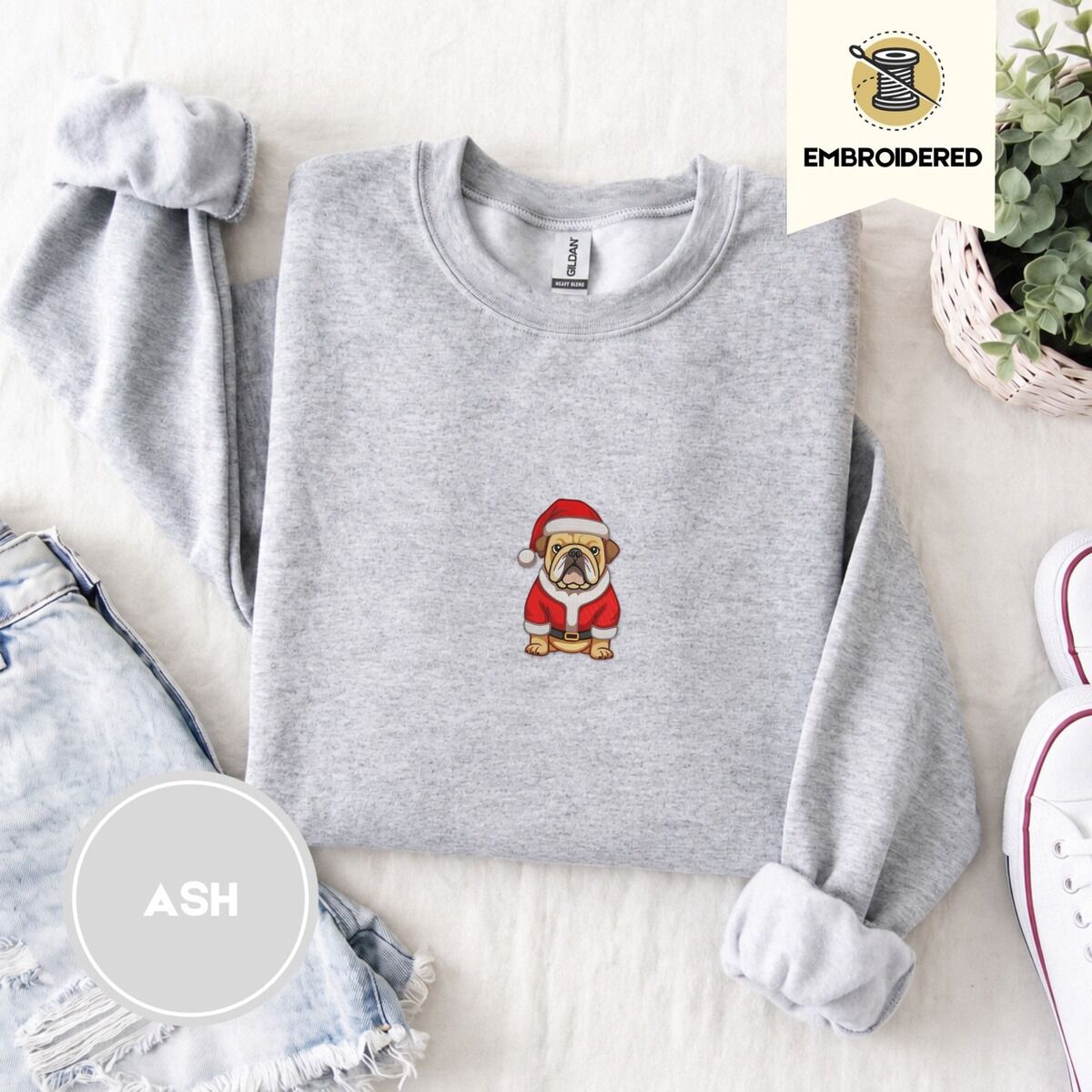 English Bulldog Christmas Sweatshirt – Ash Ash crewneck sweatshirt folded with denim shorts, white sneakers and a potted plant, embroidered with a fawn English bulldog in a red Santa suit, black belt and Santa hat
