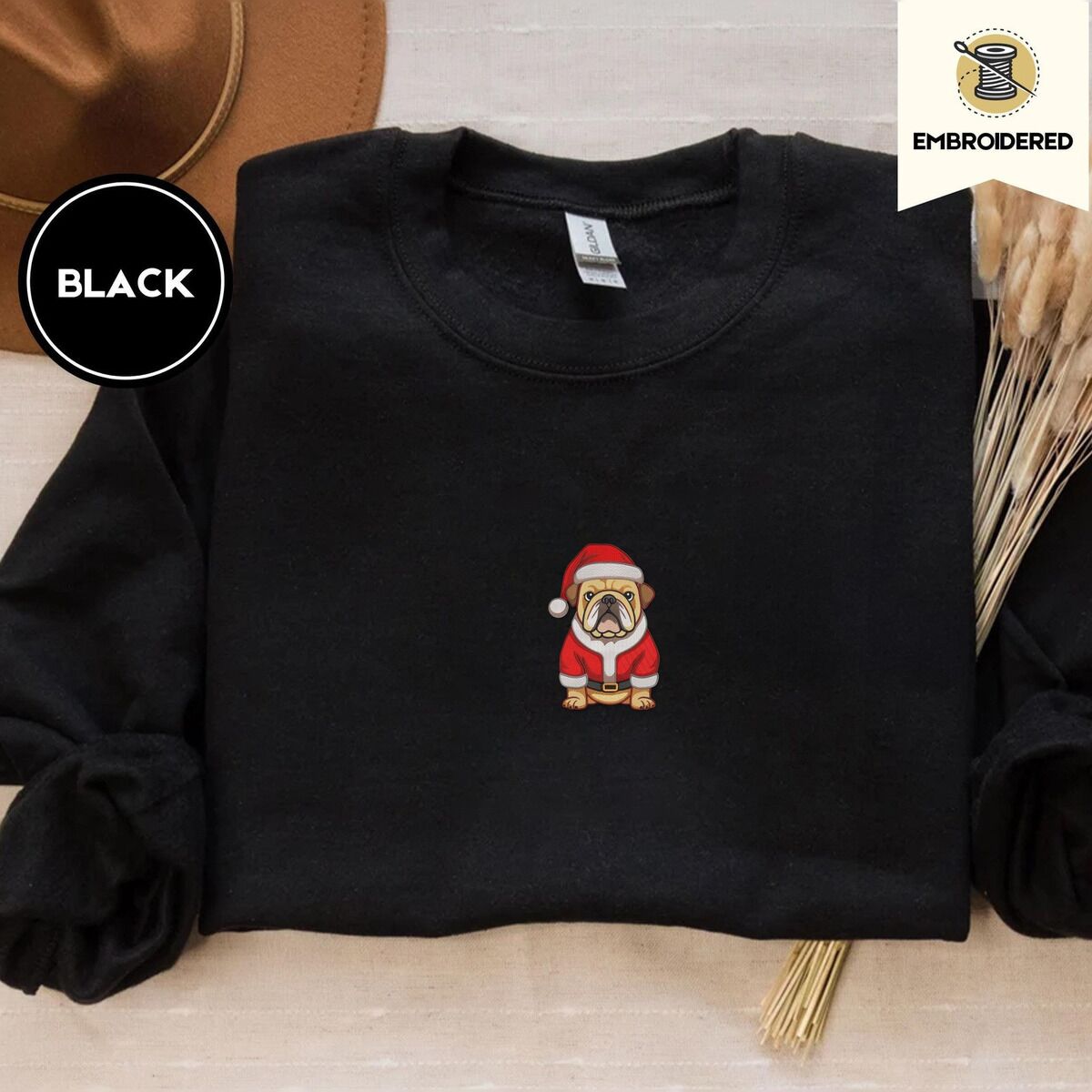 English Bulldog Christmas Sweatshirt – Black Black crewneck sweatshirt with a brown felt hat and dried bunny tail grass, embroidered with a fawn English bulldog in a red Santa suit, black belt and Santa hat