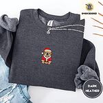 Dark Heather crewneck sweatshirt folded with ripped jeans and a silver chain necklace, embroidered with a fawn English bulldog in a red Santa suit, black belt and Santa hat