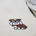 Close-up of the embroidered English bulldog with a brown and white coat, a big smile and a red collar