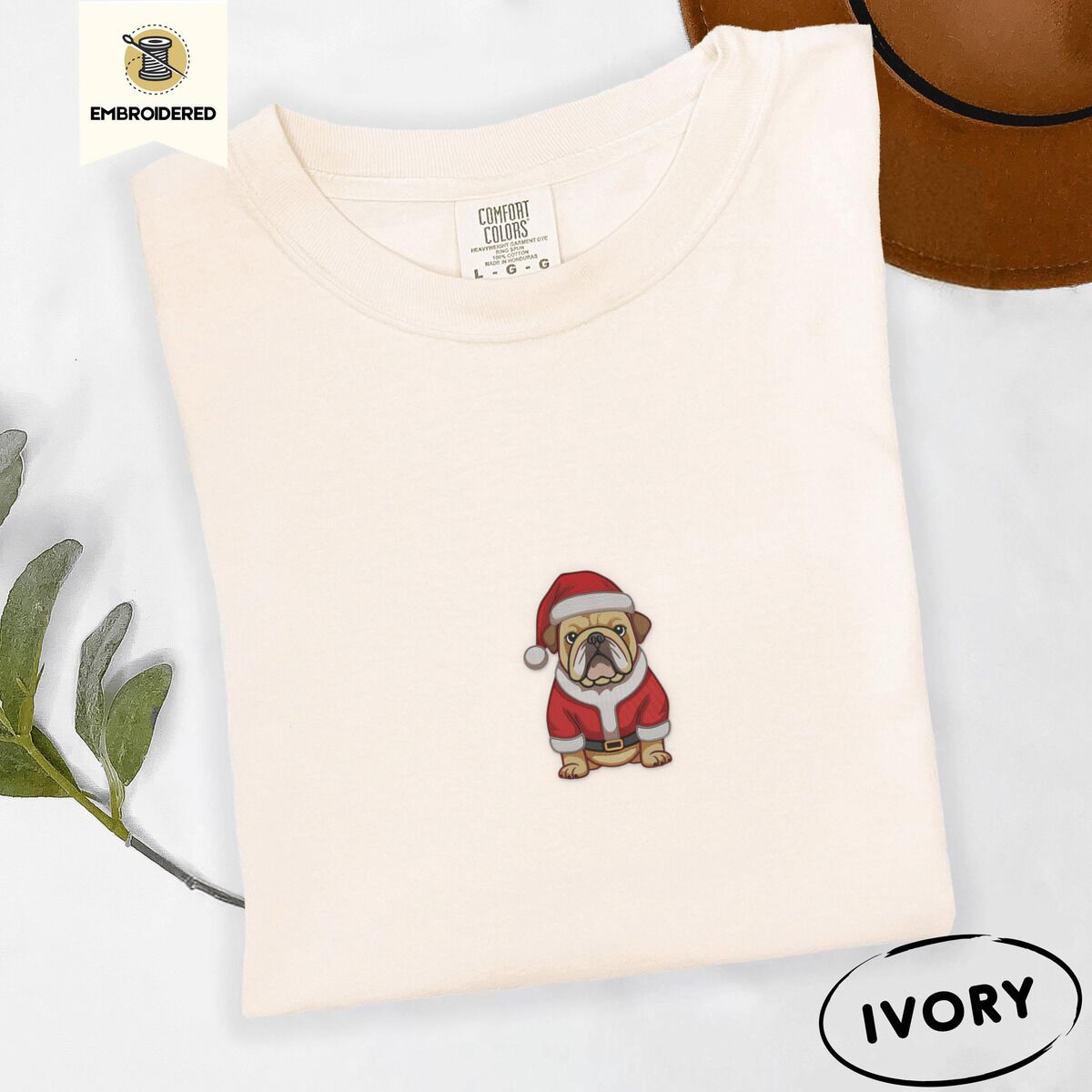 English Bulldog Santa Shirt – Ivory Ivory Comfort Colors T-shirt embroidered with a fawn English bulldog in a red Santa suit, black belt and Santa hat