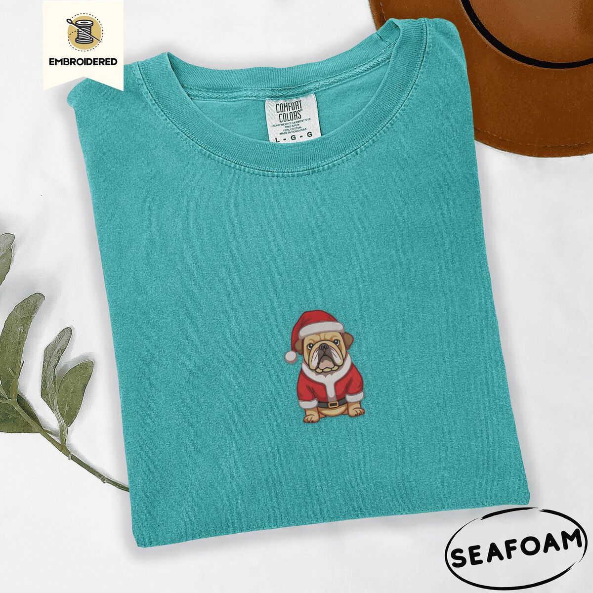 English Bulldog Santa Shirt – Seafoam Seafoam Comfort Colors T-shirt embroidered with a fawn English bulldog in a red Santa suit, black belt and Santa hat