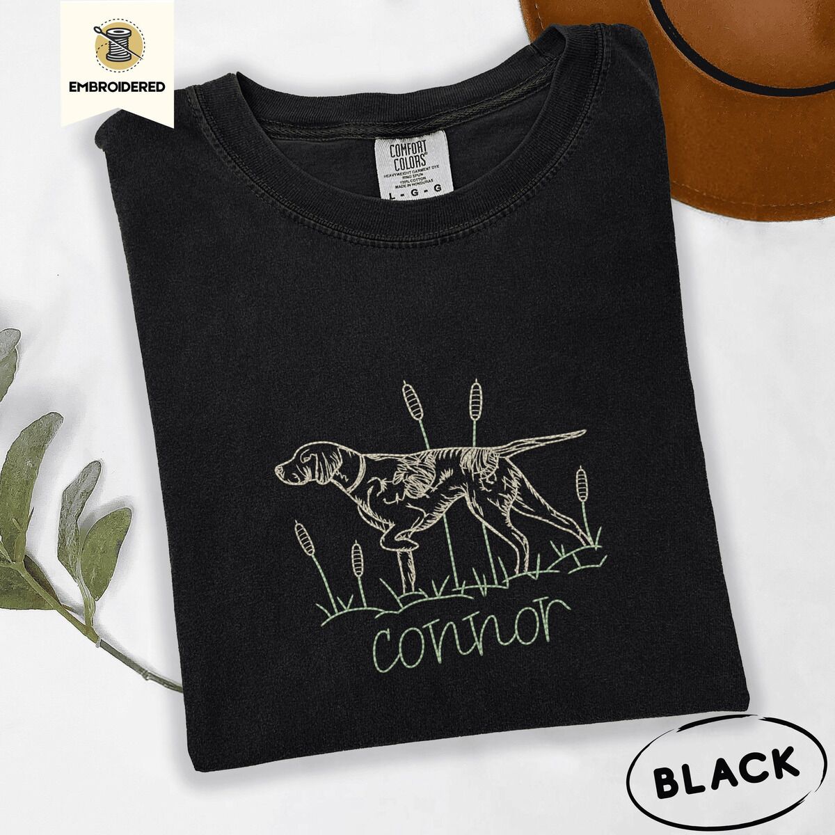 English Pointer Shirt – Black Black Comfort Colors T-shirt embroidered with a liver and white English pointer on point among cattails and grass, with an optional name stitched below