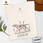 Ivory Comfort Colors T-shirt embroidered with a liver and white English pointer on point among cattails and grass, with an optional name stitched below