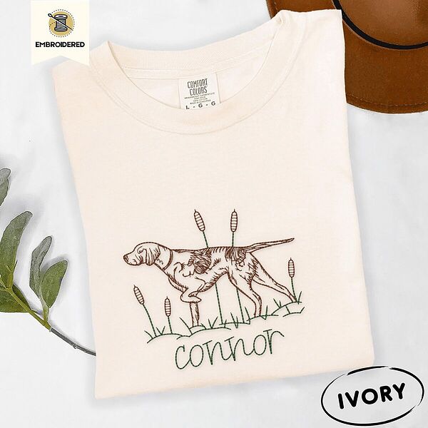 Ivory Comfort Colors T-shirt embroidered with a liver and white English pointer on point among cattails and grass, with an optional name stitched below