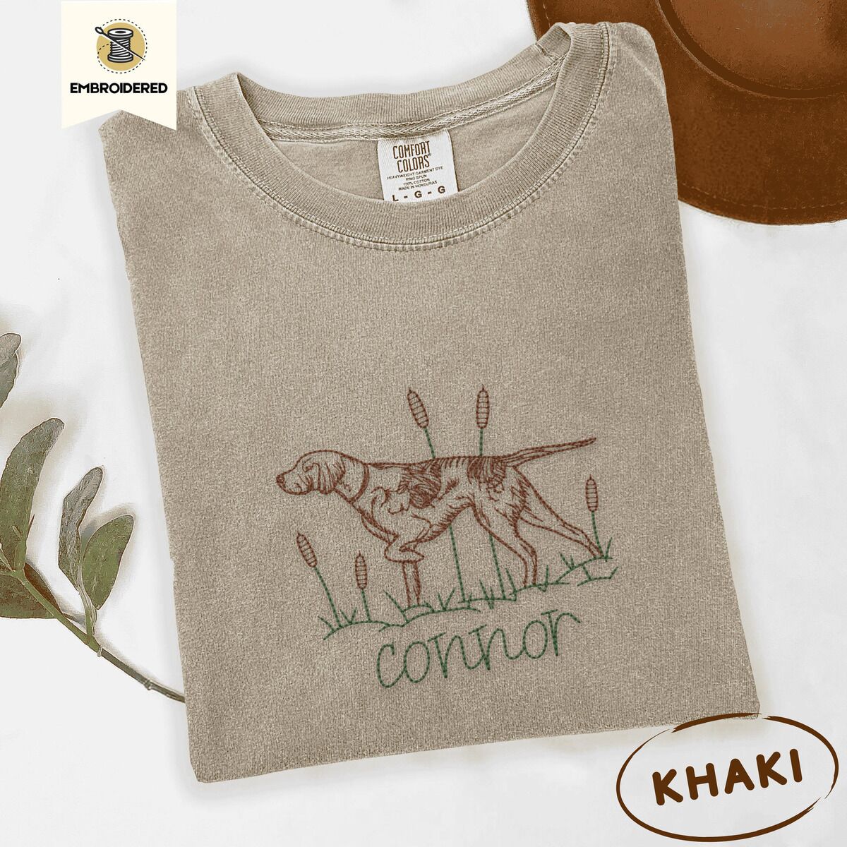 English Pointer Shirt – Khaki Khaki Comfort Colors T-shirt embroidered with a liver and white English pointer on point among cattails and grass, with an optional name stitched below