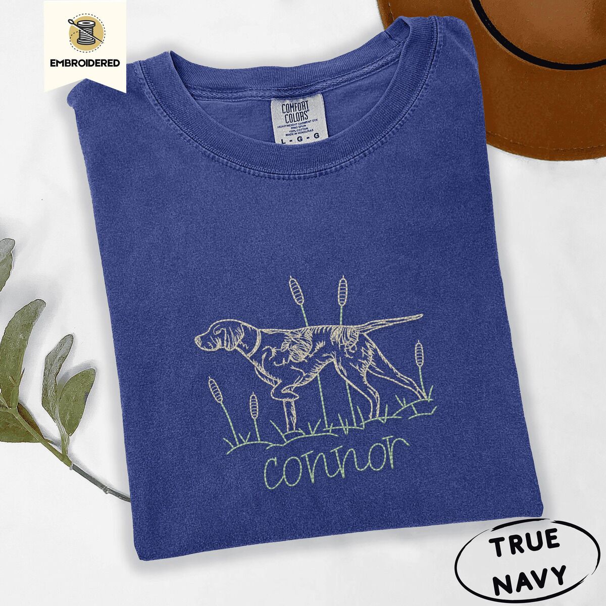 English Pointer Shirt – True Navy True Navy Comfort Colors T-shirt embroidered with a liver and white English pointer on point among cattails and grass, with an optional name stitched below