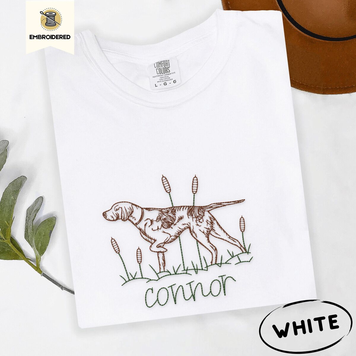 English Pointer Shirt – White White Comfort Colors T-shirt embroidered with a liver and white English pointer on point among cattails and grass, with an optional name stitched below