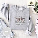 Ash crewneck sweatshirt folded with denim shorts, white sneakers and a potted plant, embroidered with a liver and white English pointer on point among cattails and grass, with an optional name stitched below