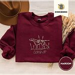 Maroon crewneck sweatshirt with a brown felt hat and dried bunny tail grass, embroidered with a liver and white English pointer on point among cattails and grass, with an optional name stitched below