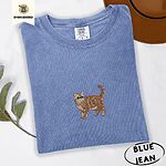 Blue Jean Comfort Colors T-shirt embroidered with an orange tabby Exotic Shorthair cat standing in profile with a flat face, round black eyes and a curled tail