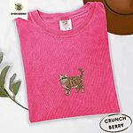 Crunchberry Comfort Colors T-shirt embroidered with an orange tabby Exotic Shorthair cat standing in profile with a flat face, round black eyes and a curled tail