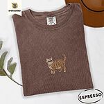 Espresso Comfort Colors T-shirt embroidered with an orange tabby Exotic Shorthair cat standing in profile with a flat face, round black eyes and a curled tail