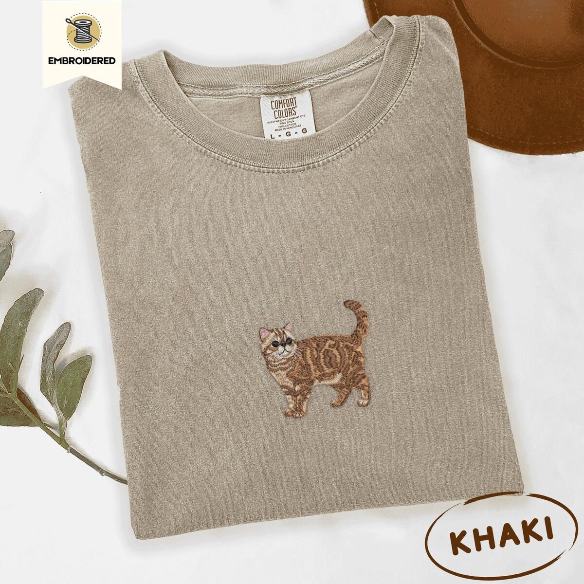 Exotic Shorthair Shirt – Khaki Khaki Comfort Colors T-shirt embroidered with an orange tabby Exotic Shorthair cat standing in profile with a flat face, round black eyes and a curled tail