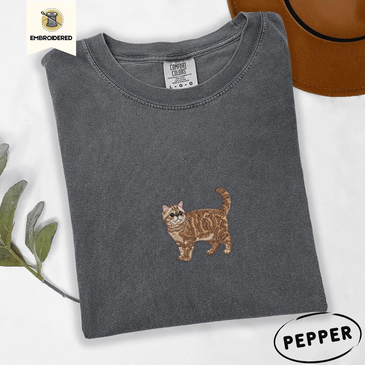 Exotic Shorthair Shirt – Pepper Pepper Comfort Colors T-shirt embroidered with an orange tabby Exotic Shorthair cat standing in profile with a flat face, round black eyes and a curled tail