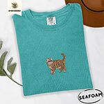 Seafoam Comfort Colors T-shirt embroidered with an orange tabby Exotic Shorthair cat standing in profile with a flat face, round black eyes and a curled tail