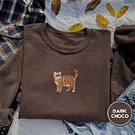 Dark Chocolate Exotic Shorthair sweatshirt on a plaid flannel shirt with yellow autumn leaves and denim shorts, with a mini embroidered orange tabby cat centered on the chest