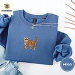 Indigo Blue Exotic Shorthair sweatshirt folded with light jeans and dried twigs, with a mini embroidered orange tabby cat centered on the chest