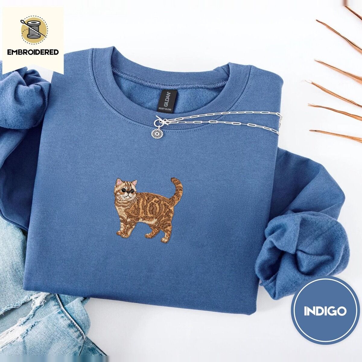 Exotic Shorthair Sweatshirt – Indigo Blue Indigo Blue Exotic Shorthair sweatshirt folded with light jeans and dried twigs, with a mini embroidered orange tabby cat centered on the chest