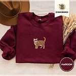 Maroon Exotic Shorthair sweatshirt with a brown felt hat and dried bunny tail grass, with a mini embroidered orange tabby cat centered on the chest