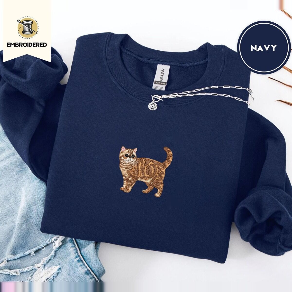 Exotic Shorthair Sweatshirt – Navy Navy Exotic Shorthair sweatshirt folded with ripped jeans and a silver chain necklace, with a mini embroidered orange tabby cat centered on the chest