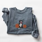Dark Heather crewneck sweatshirt laid flat with a rolled cuff, embroidered with a black and white tuxedo pit bull sitting between two orange pumpkins