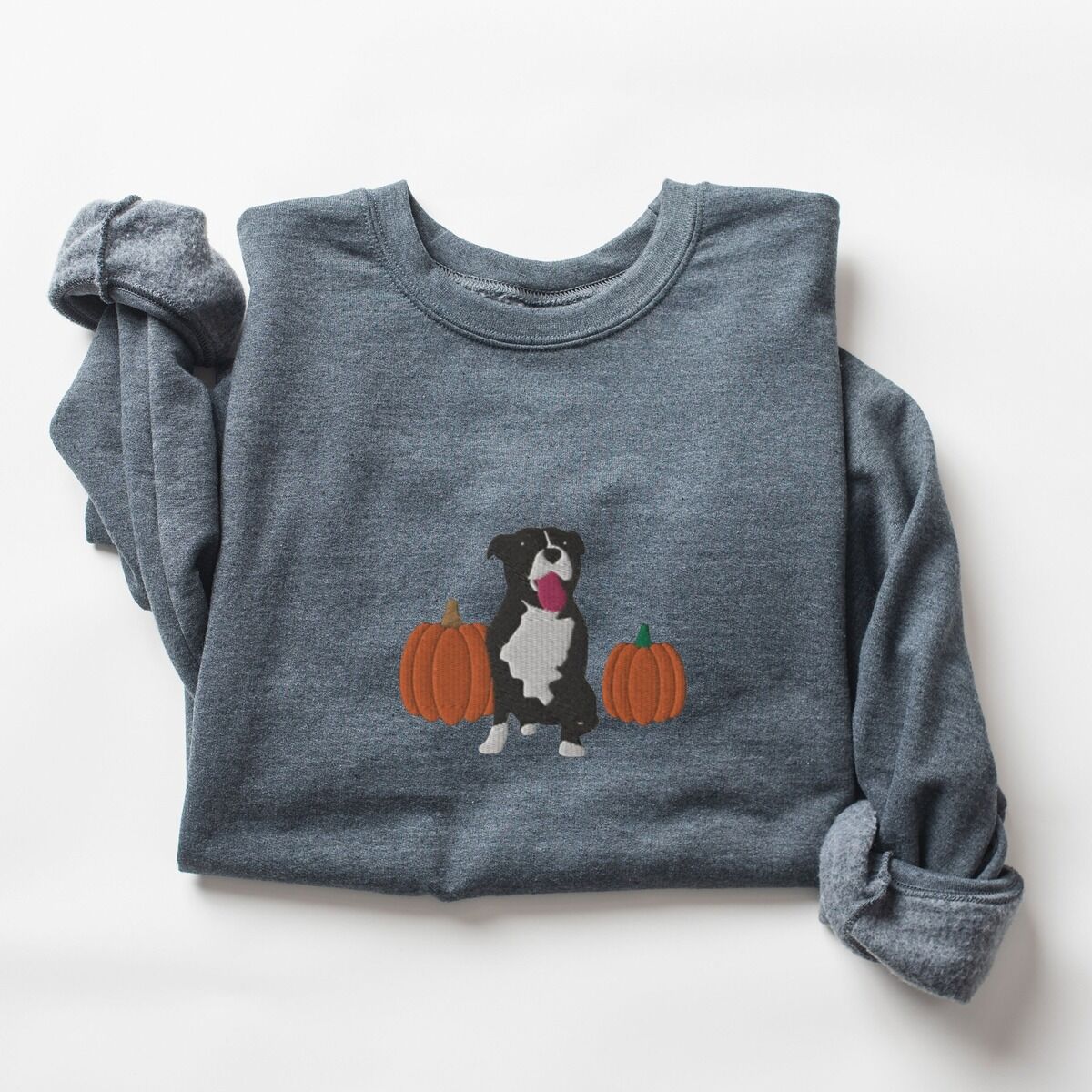Fall Pitbull Sweatshirt – Dark Heather Dark Heather crewneck sweatshirt laid flat with a rolled cuff, embroidered with a black and white tuxedo pit bull sitting between two orange pumpkins