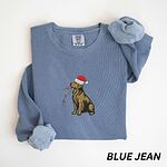 Blue Jean crewneck sweatshirt laid flat, embroidered with a golden retriever in a red Santa hat carrying a strand of colored bulbs