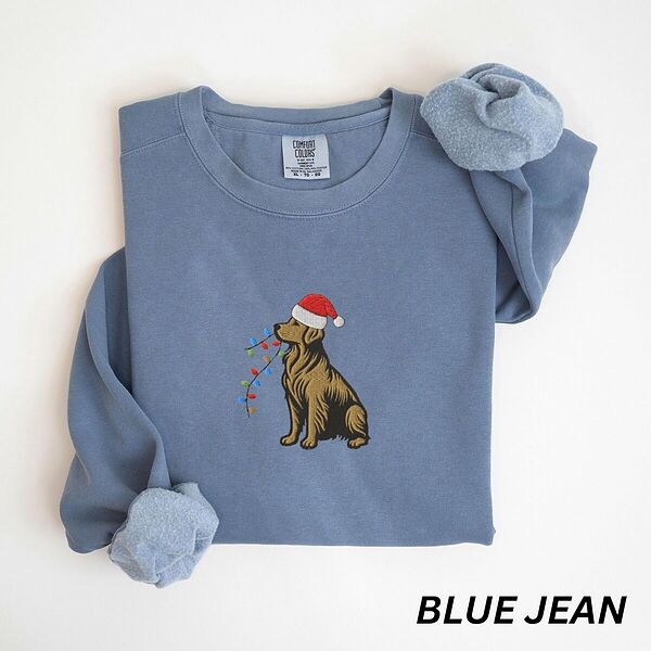 Blue Jean crewneck sweatshirt laid flat, embroidered with a golden retriever in a red Santa hat carrying a strand of colored bulbs