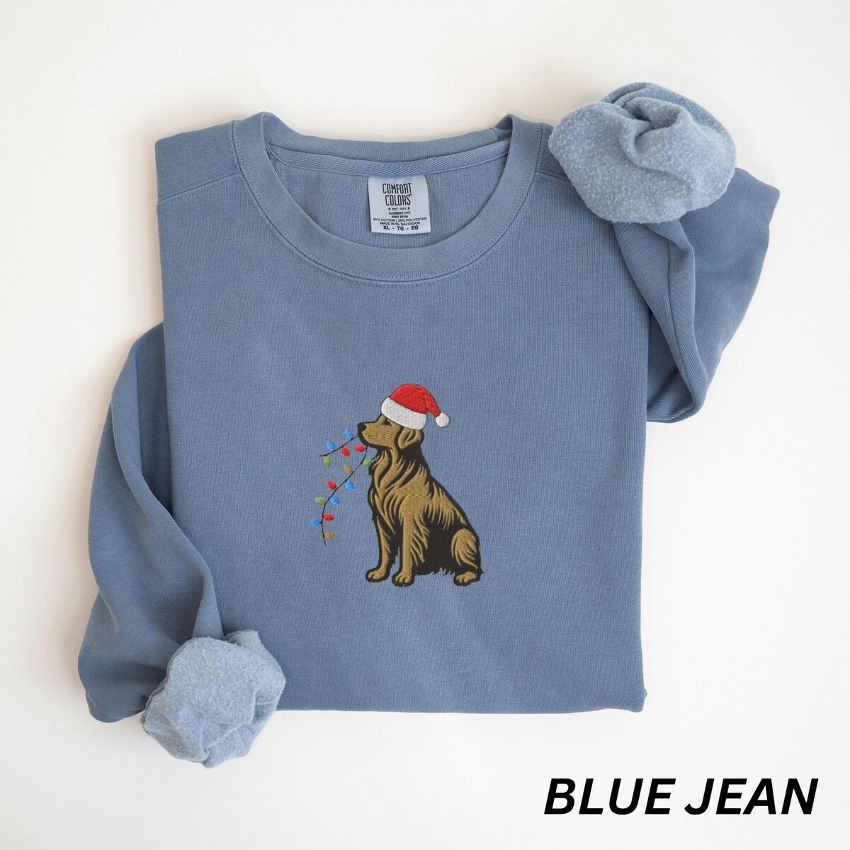 Festive Golden Retriever Sweatshirt – Blue Jean Blue Jean crewneck sweatshirt laid flat, embroidered with a golden retriever in a red Santa hat carrying a strand of colored bulbs