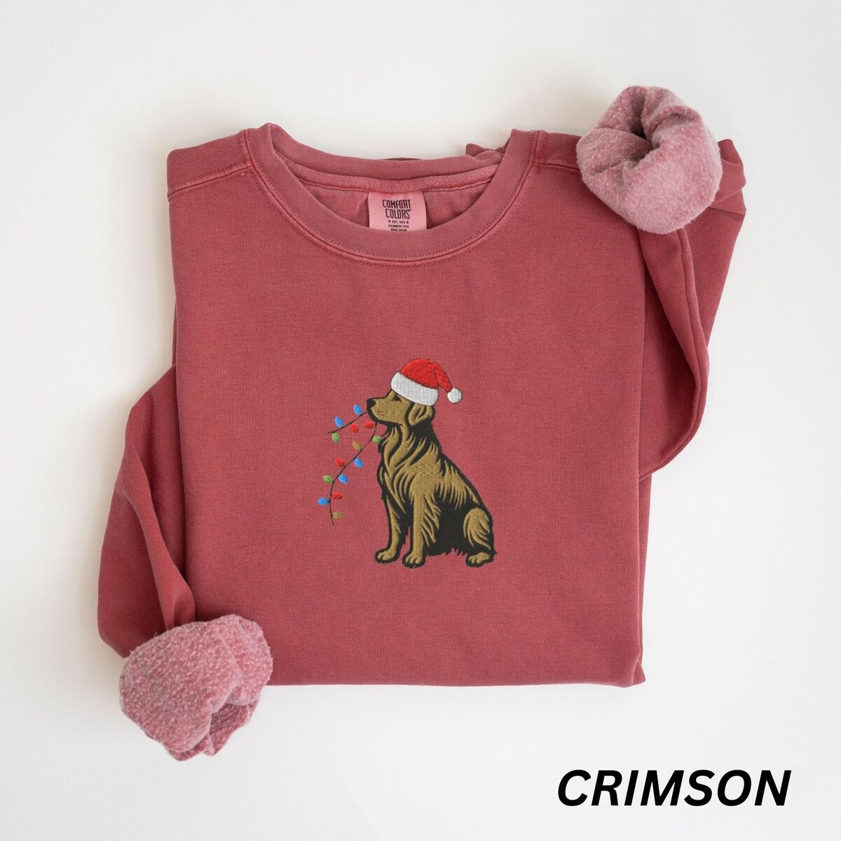 Festive Golden Retriever Sweatshirt – Crimson Crimson crewneck sweatshirt laid flat, embroidered with a sitting golden retriever in a Santa hat holding a strand of Christmas lights