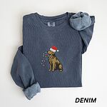 Denim crewneck sweatshirt laid flat, embroidered with a golden retriever in a Santa hat with a light strand in its mouth